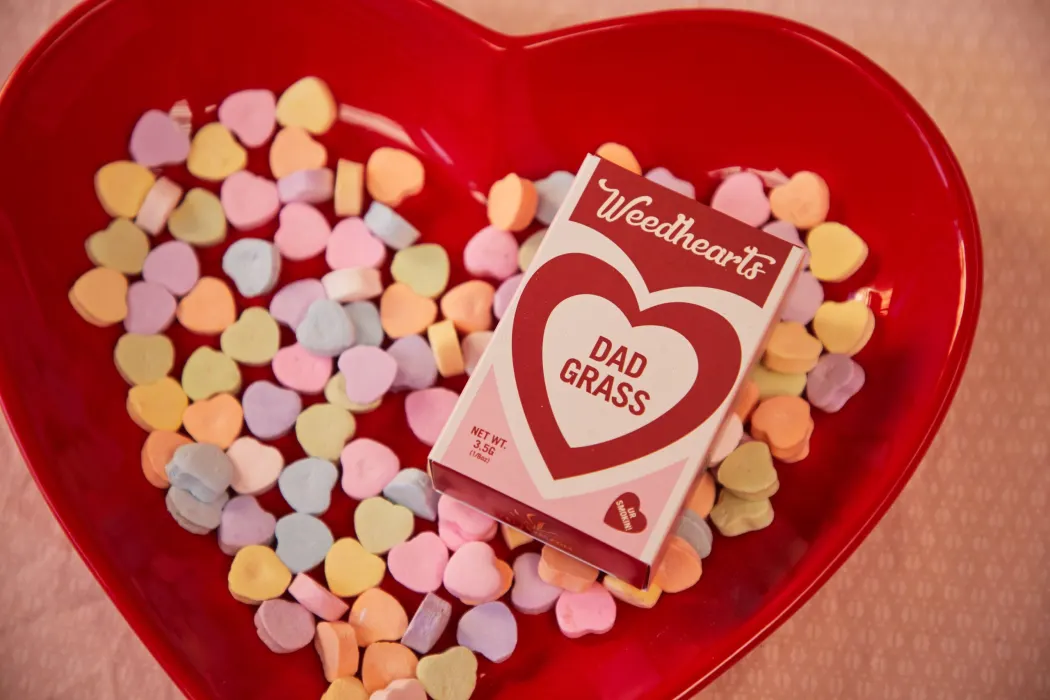 Candy hearts in a heart-shaped dish with a "Dad Grass" cannabis product, for enhancing intimacy with cannabis.