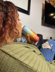 A person sipping a can of liquid cannabis edibles while relaxing on a sofa.